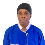 Portrait of a healthcare worker wearing a blue scrub top with white trim and a black cap, facing the camera; 'Excellence Center' logo visible on the uniform.