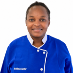 Portrait of a smiling Black woman in blue medical scrubs with white trim against a white background, embroidery reading 'Excellence Center' on the chest