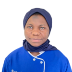 Portrait of a woman wearing a navy hijab and blue scrubs with white piping, facing the camera against a white background (staff photo for Excellence Center).