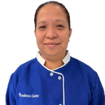 Smiling staff member in a blue uniform with white trim and the 'Excellence Center' logo on the chest.