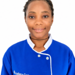 Portrait of a smiling woman in a blue chef-style uniform with white trim, wearing a black choker, and 'Excellence Center' logo visible on the chest.
