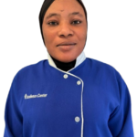 Portrait of a woman in a blue uniform with white trim and a hijab, wearing a top that reads 'Excellence Center'.