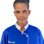 Front-facing portrait of a woman with dark hair tied in a bun, wearing a blue uniform with a white collar, looking at the camera.