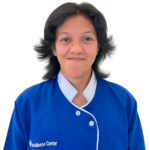 Woman staff member in a blue uniform with white trim, smiling at the camera; 'Excellence Center' logo visible on the chest area.
