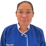 Portrait of a smiling woman in a blue uniform with white trim, facing camera (employee at a clinic).