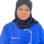 Portrait of a woman wearing a blue uniform and a black hijab, facing the camera; logo reads 'Excellence Center' on the chest.