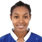 Portrait of a smiling Black woman in a blue uniform with a white collar against a white background, looking straight at the camera.