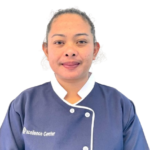 Portrait of a woman in a navy chef’s jacket with white piping, facing the camera; the jacket reads “Excellence Center” on the left.