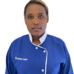 Portrait of a woman in a blue chef-style uniform with white trim and 'Excellence Center' embroidery, facing the camera against a plain background.