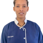Portrait of a person wearing a blue front-buttoned uniform with a white collar, facing the camera with a neutral expression.