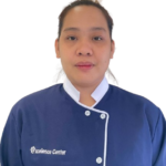 Portrait of a staff member facing the camera, wearing a blue chef-style uniform with white trim and the 'Excellence Center' logo on the chest.