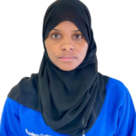 Woman wearing a black hijab and blue uniform with 'Excellence Center' logo, looking at the camera against a white background.
