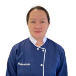 Woman facing camera in a blue chef/journal uniform with white trim and logo on the left chest area reading 'Excellence Center' (informational portrait).
