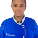Portrait of a staff member wearing a blue uniform with white trim, standing against a white background; logo reads 'Excellence Center' on the chest.