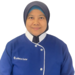 Smiling woman in a blue uniform with white trim and a dark hijab; logo 'Excellence Center' on the chest.