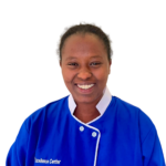 Smiling woman in a blue uniform with white trim, standing against a white background (Excellence Center logo visible).