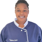 Person in a navy uniform with white trim, smiling at the camera; 'Excellence Center' logo on the chest.