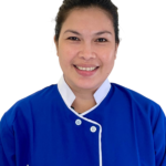 Smiling woman in a blue uniform with white trim, standing against a white background; Excellence Center logo visible on the chest area.