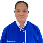 Portrait of a person facing camera wearing a blue uniform with white trim and a visible 'Excellence Center' logo, smiling slightly.